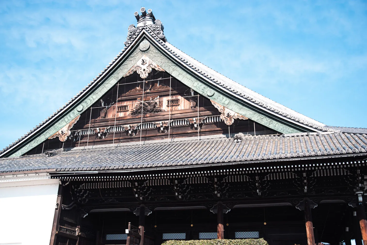 青空の下で、伝統的な木造建築の大きな屋根を正面から写した写真