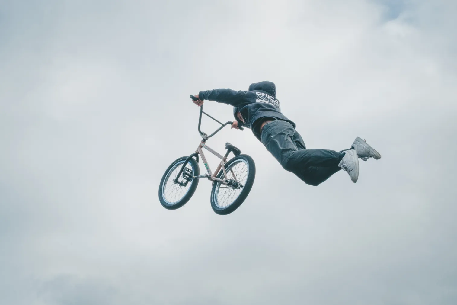 曇り空を背景に、自転車でジャンプする人物を写した写真